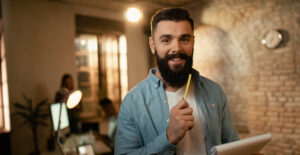 migrar MEI para ME - empreendedor sorrindo segurando lápis em escritório